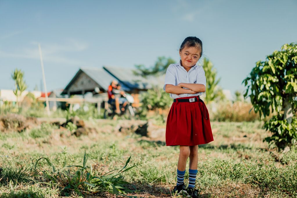 Karunia stands with her school uniform on, crossing her arms and smiling infront of her school.